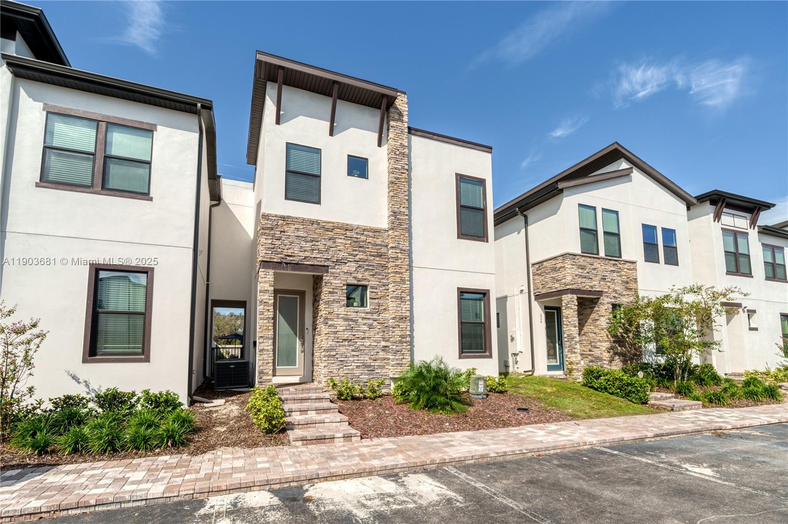 The exterior of a modern townhouse features white stucco walls, stone veneer accents, and dark trim — 232 Villa Domani, Davenport FL 33896, DAVENPORT, FL