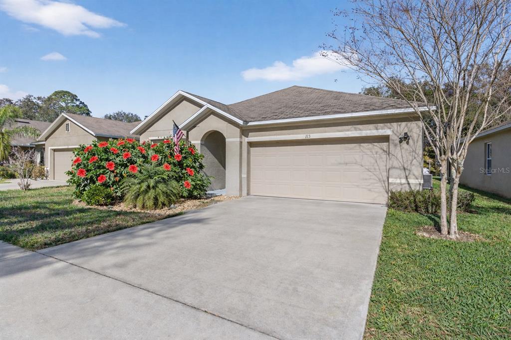 A single-story house with a beige stucco exterior, a two-car garage, and red flowering bushes — 113 FISHERMANS COVE DRIVE, EDGEWATER, FL
