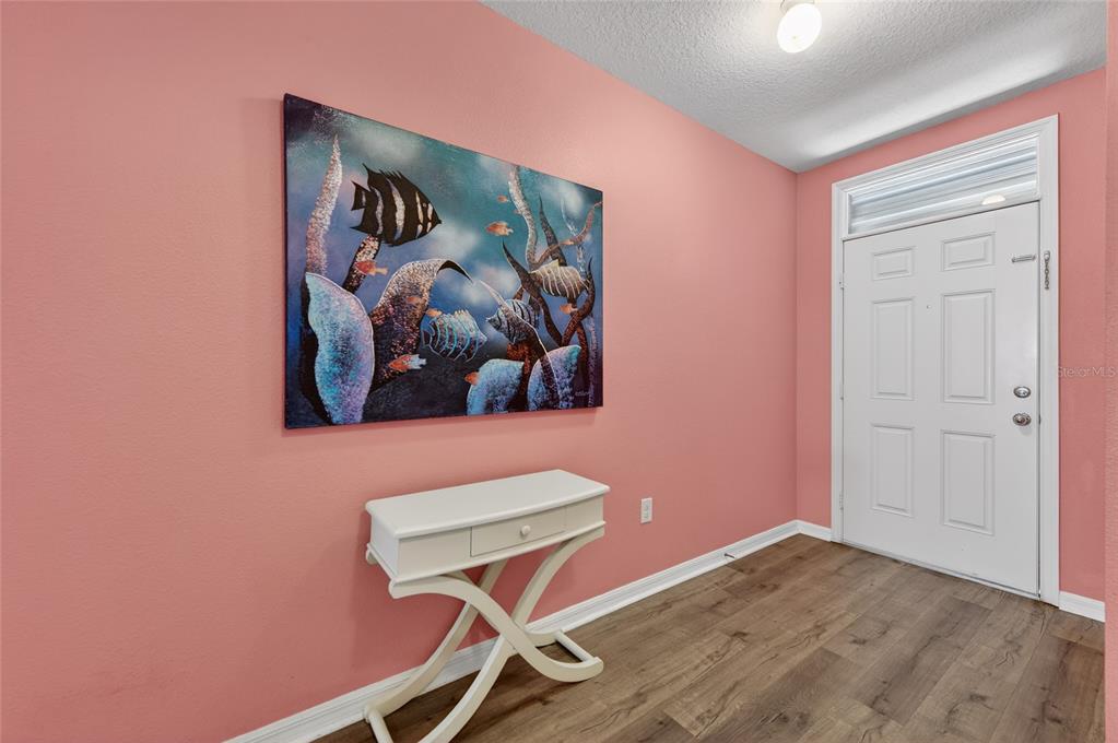 An entryway features pink walls, a white console table, a fish painting, and wood flooring — 113 FISHERMANS COVE DRIVE, EDGEWATER, FL