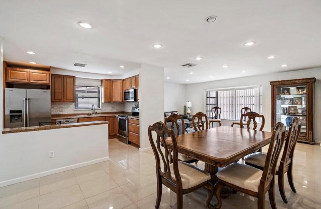 An open-concept kitchen and dining area with wooden cabinets, stainless appliances, and tile flooring — 6089 Glentree Lane, FL 33463, FL