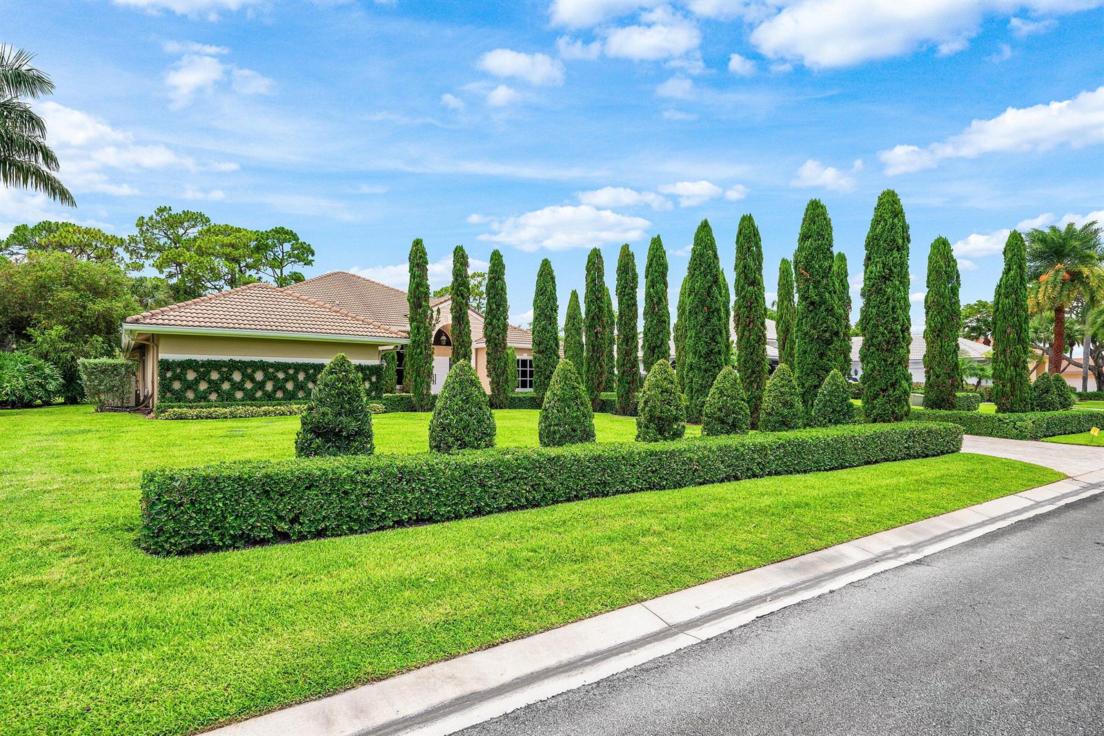 A single-story house with a manicured lawn, tall cypress trees, and a low hedge — 1697 Mayacoo Lakes Boulevard, West Palm Beach FL 33411, WEST PALM BEACH, FL