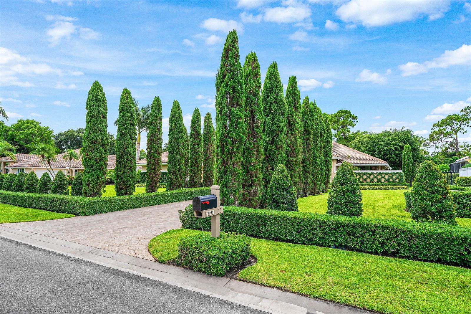 A paved driveway leads to a house partially obscured by tall, manicured cypress trees and hedges — 1697 Mayacoo Lakes Boulevard, West Palm Beach FL 33411, WEST PALM BEACH, FL