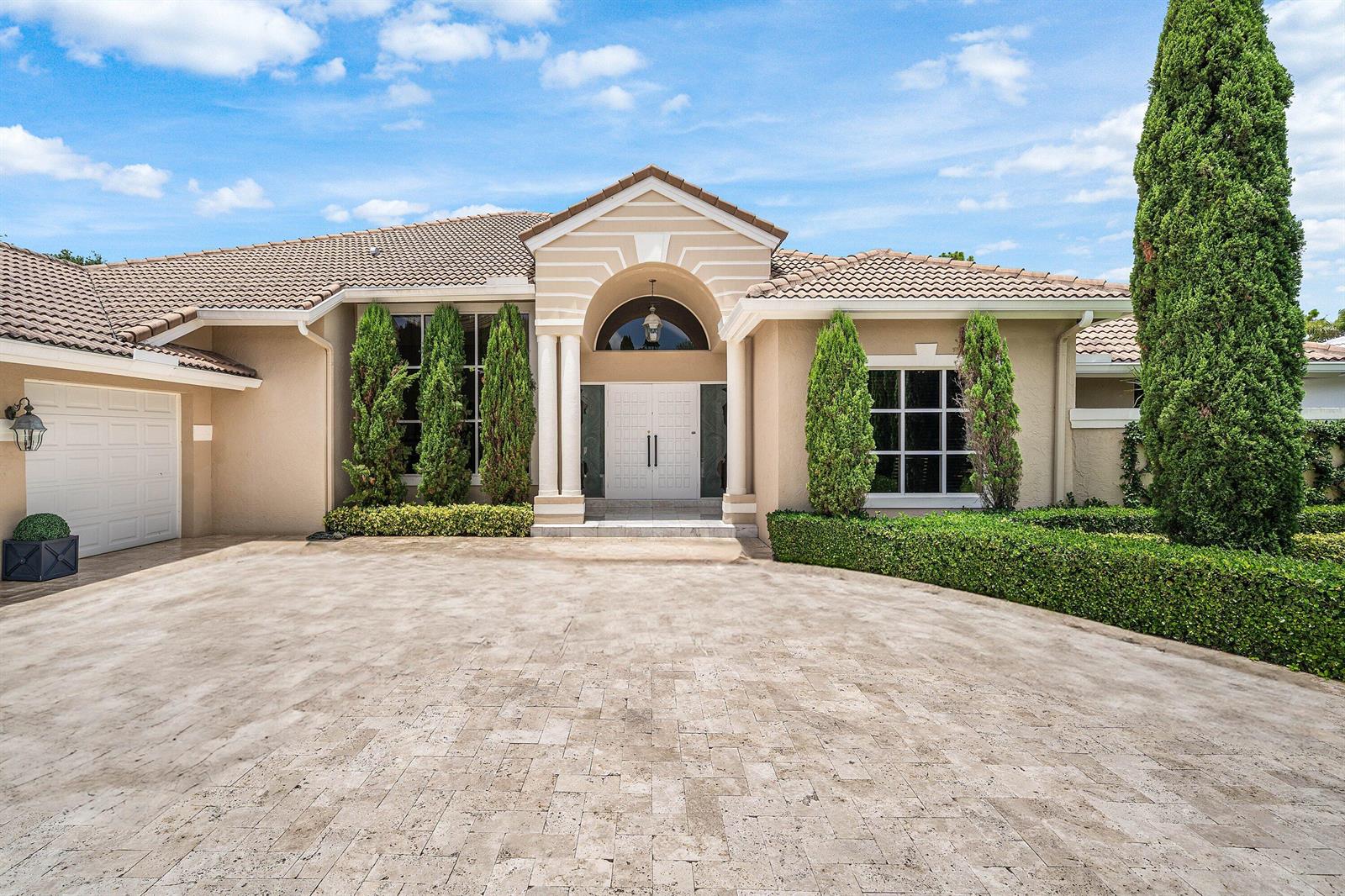 A beige single-story house features a stone-paved driveway, arched entryway, and manicured landscaping — 1697 Mayacoo Lakes Boulevard, West Palm Beach FL 33411, WEST PALM BEACH, FL