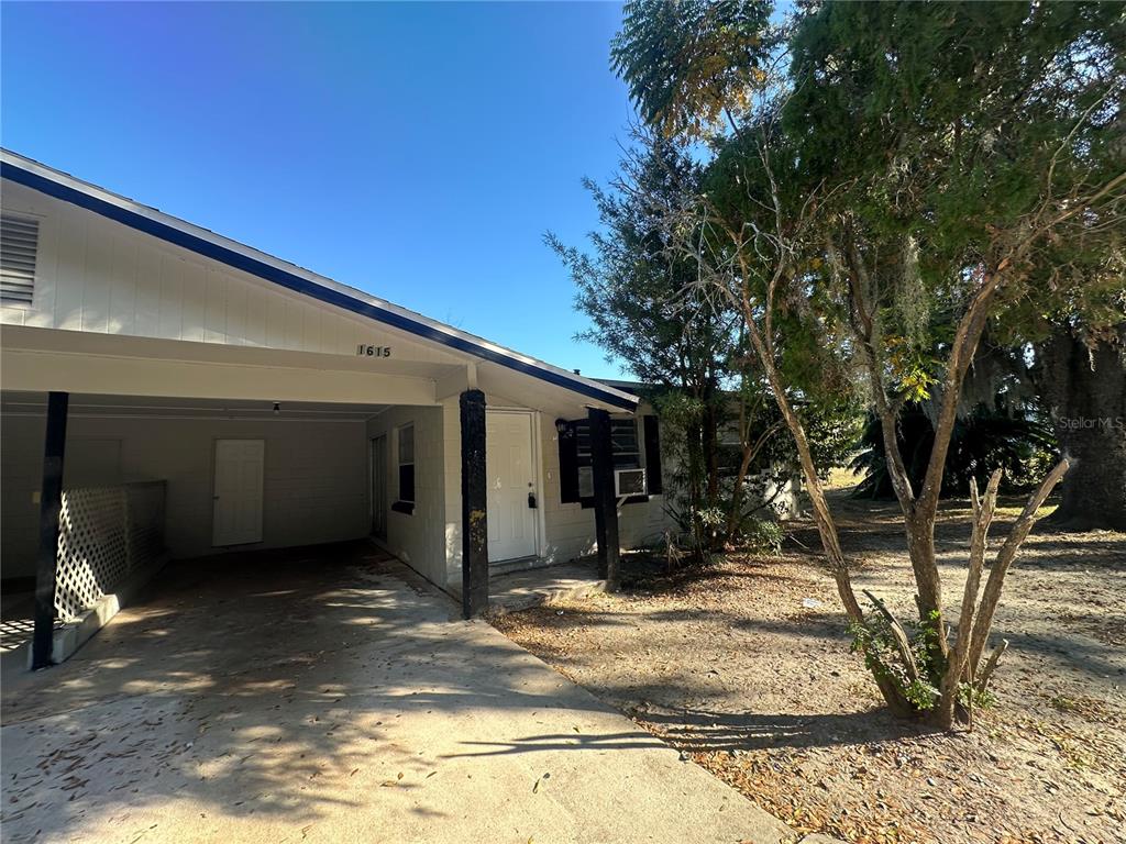 A single-story house exterior features a concrete driveway, a carport, and a white front door — 1615 N NEW YORK AVENUE, LAKELAND, FL