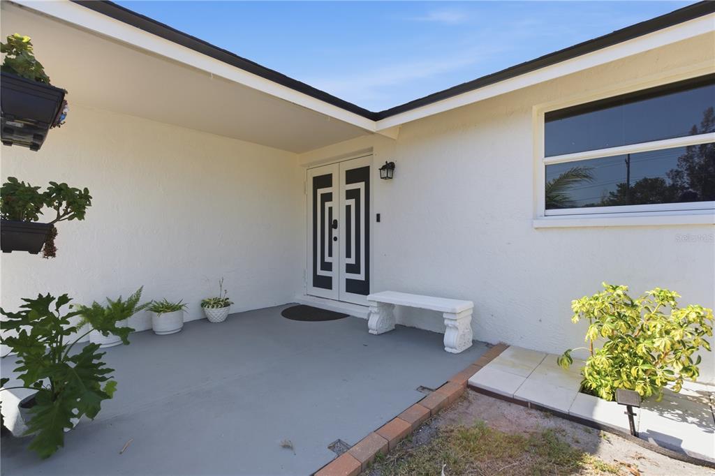 A white house exterior features a covered entryway with a double door and a bench — 601 GOLF AND SEA BOULEVARD, APOLLO BEACH, FL