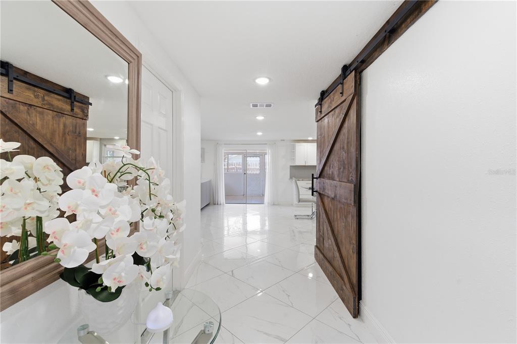 A hallway with white marble floors leads to a bright room with sliding glass doors — 601 GOLF AND SEA BOULEVARD, APOLLO BEACH, FL