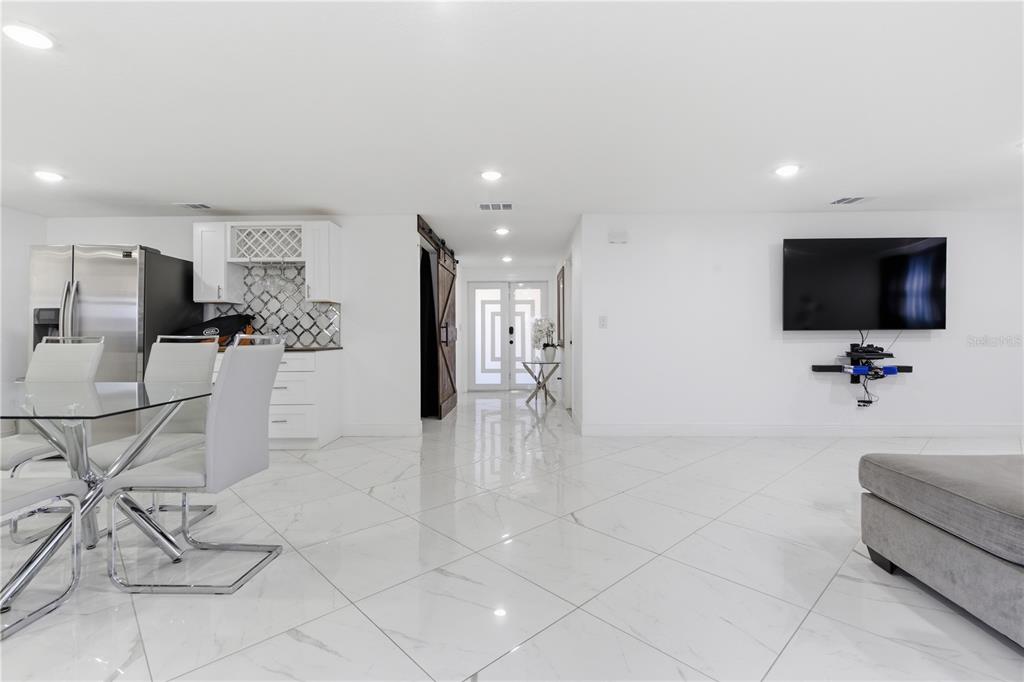 A bright, open-concept room features white marble tile floors, a dining area, and a television — 601 GOLF AND SEA BOULEVARD, APOLLO BEACH, FL
