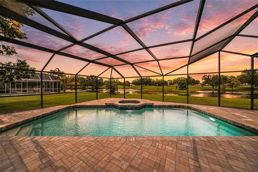 A swimming pool and spa enclosed by a screen cage overlook a pond at sunset — 6221 99TH STREET E, BRADENTON, FL