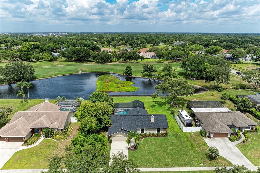 An aerial view shows three suburban houses with pools near a pond and golf course — 6221 99TH STREET E, BRADENTON, FL