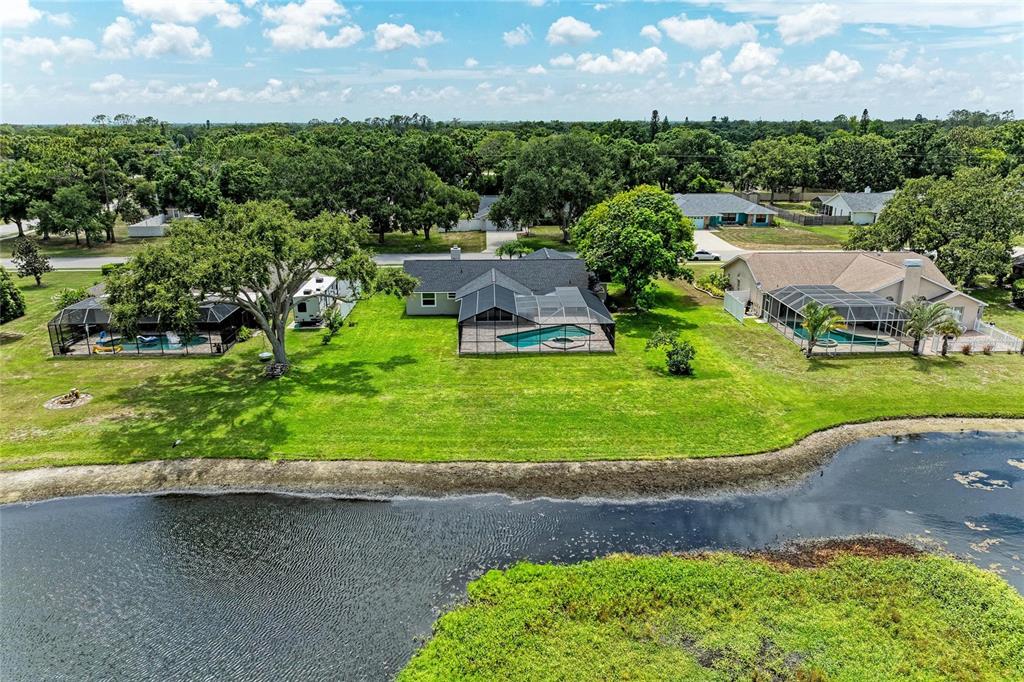 An aerial view shows three houses with screened-in pools situated along a grassy waterfront lot — 6221 99TH STREET E, BRADENTON, FL