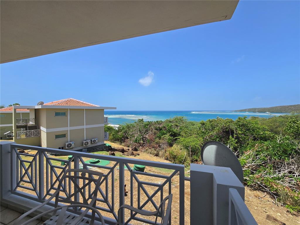 A balcony view overlooks a neighboring building, lush vegetation, and the ocean under a clear sky — Punta Canero,BO. Frailes COSTA BONITA UNIT 1702, CULEBRA, PR