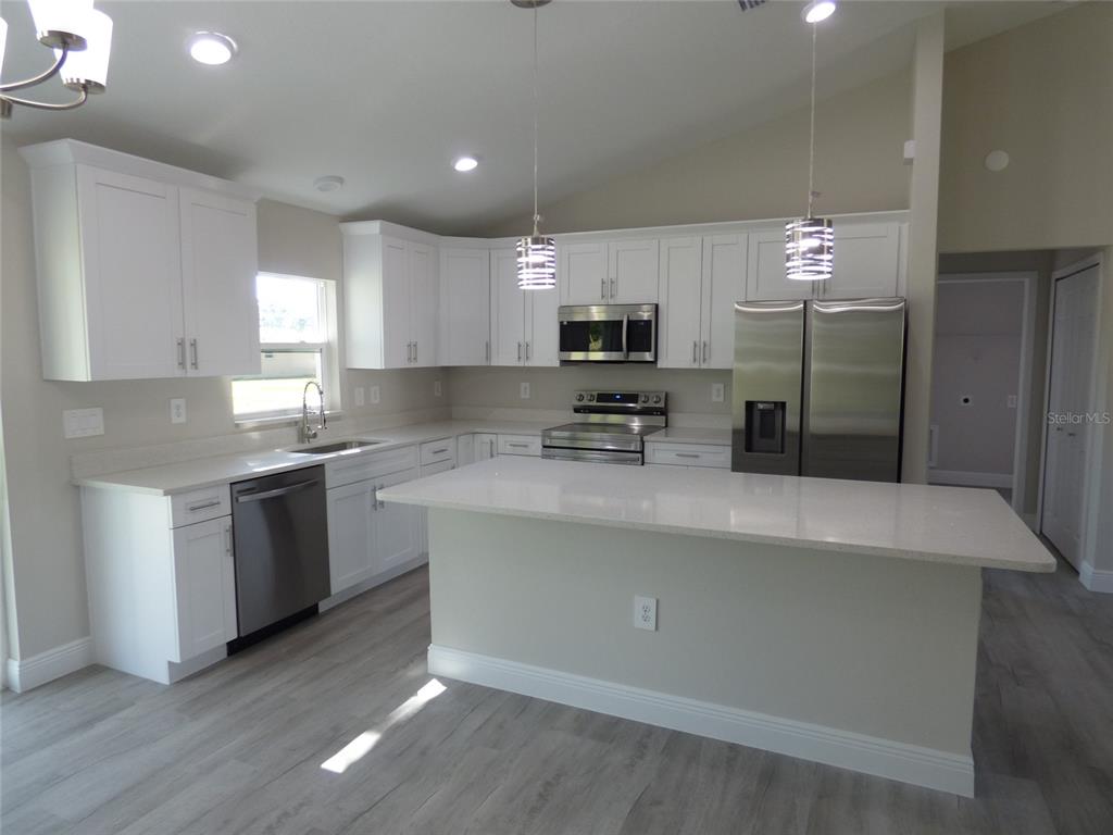 A modern kitchen features white cabinets, stainless steel appliances, a center island, and light flooring — 7959 N INDEPENDENCE WAY, CITRUS SPRINGS, FL