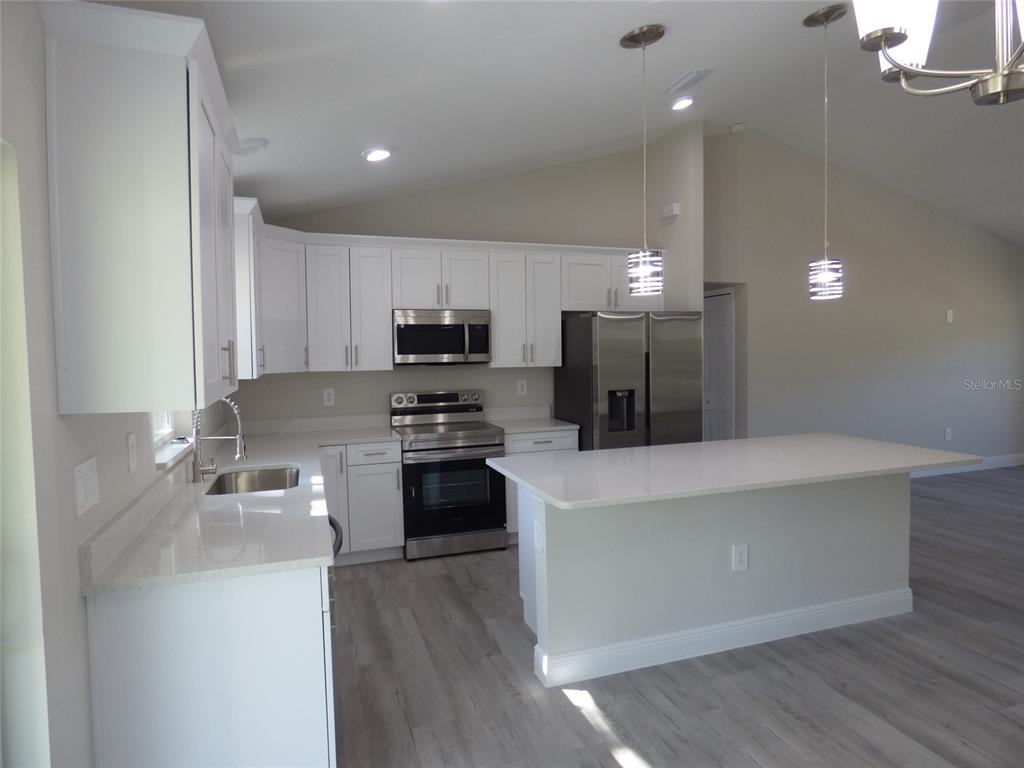 A kitchen features white cabinets, stainless steel appliances, a quartz island, and light wood flooring — 7959 N INDEPENDENCE WAY, CITRUS SPRINGS, FL