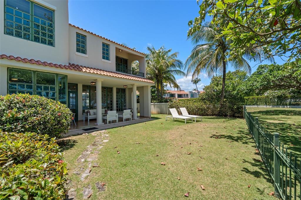 Two chairs sit on a grassy lawn under a tree overlooking the ocean and fence — 57 DORADO REEF, DORADO, PR