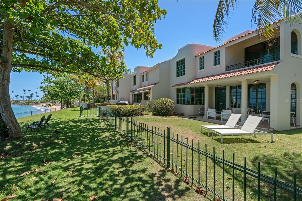 A grassy backyard with lounge chairs overlooks the ocean next to a multi-story building — 57 DORADO REEF, DORADO, PR