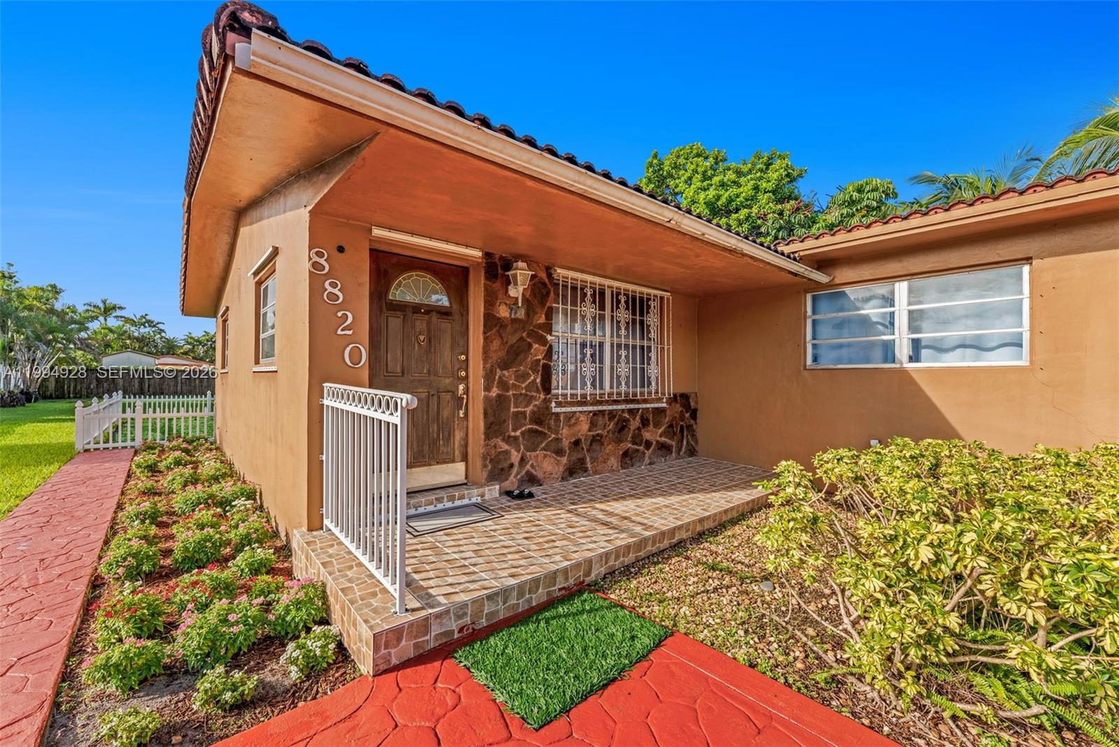 The exterior of a tan house features a stone-accented entryway, a tiled porch, and landscaping — 8820 SW 27th St, Miami FL 33165, MIAMI, FL