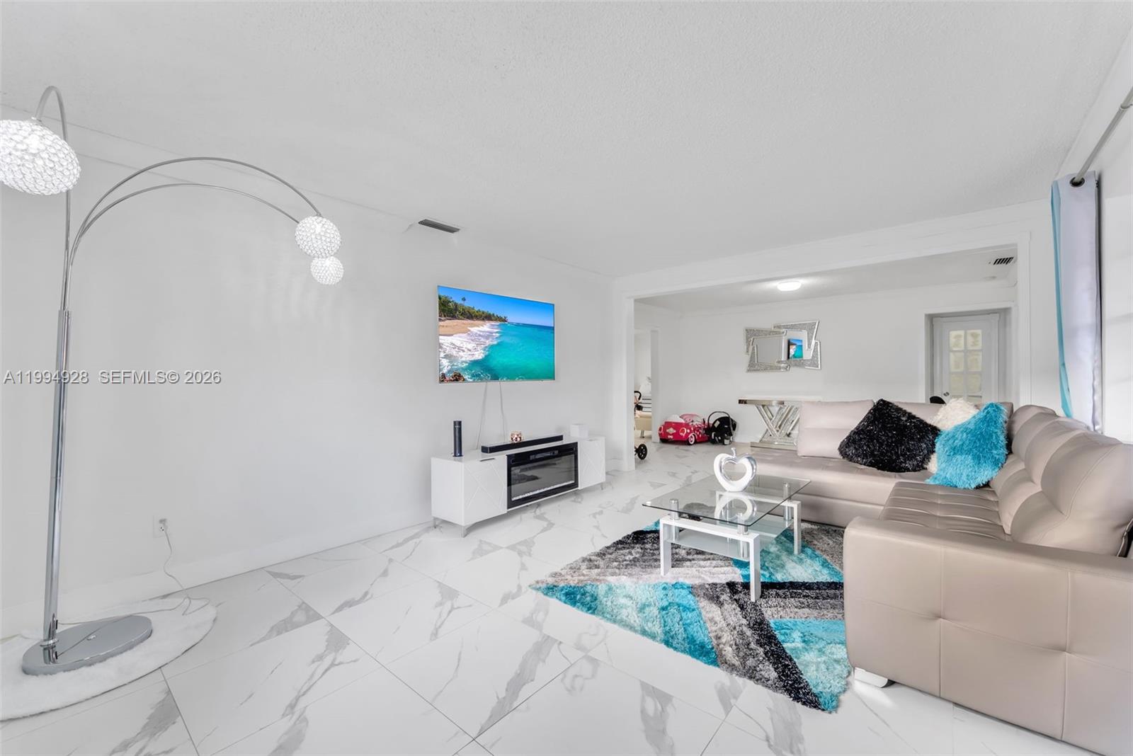 A living room features white marble-look tile floors, a wall-mounted television, and a sectional sofa — 8820 SW 27th St, Miami FL 33165, MIAMI, FL