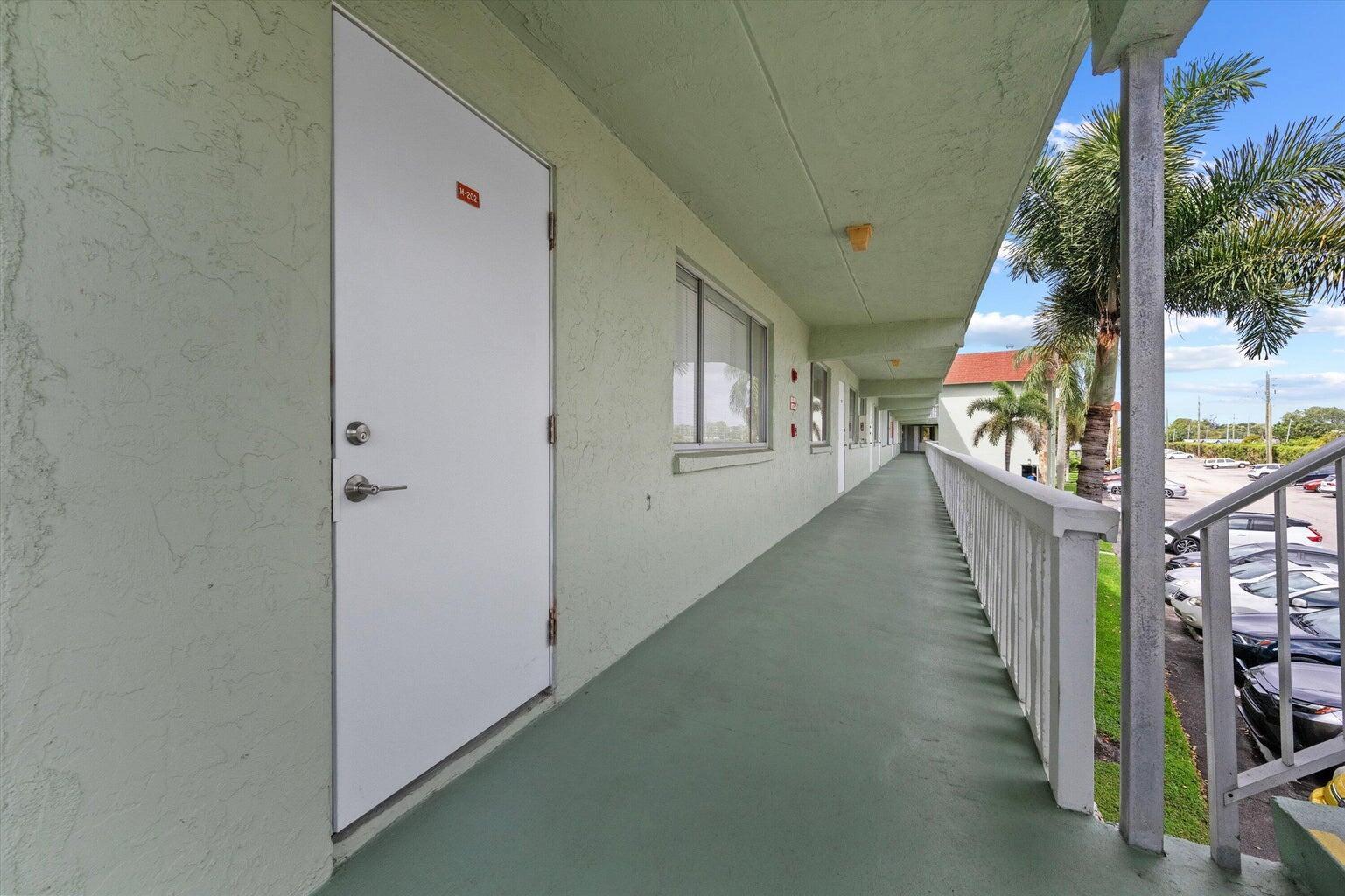 An exterior walkway with a white door leads along a building with a green floor — 3300 Springdale Boulevard # 202, Palm Springs FL 33461, PALM SPRINGS, FL