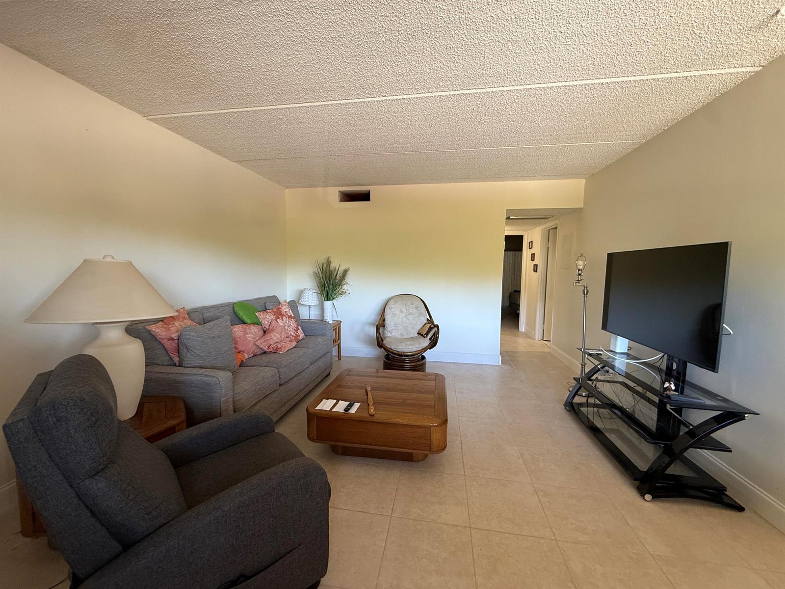A living room features a gray sofa, a recliner, a wooden coffee table, and a television — 3300 Springdale Boulevard # 202, Palm Springs FL 33461, PALM SPRINGS, FL