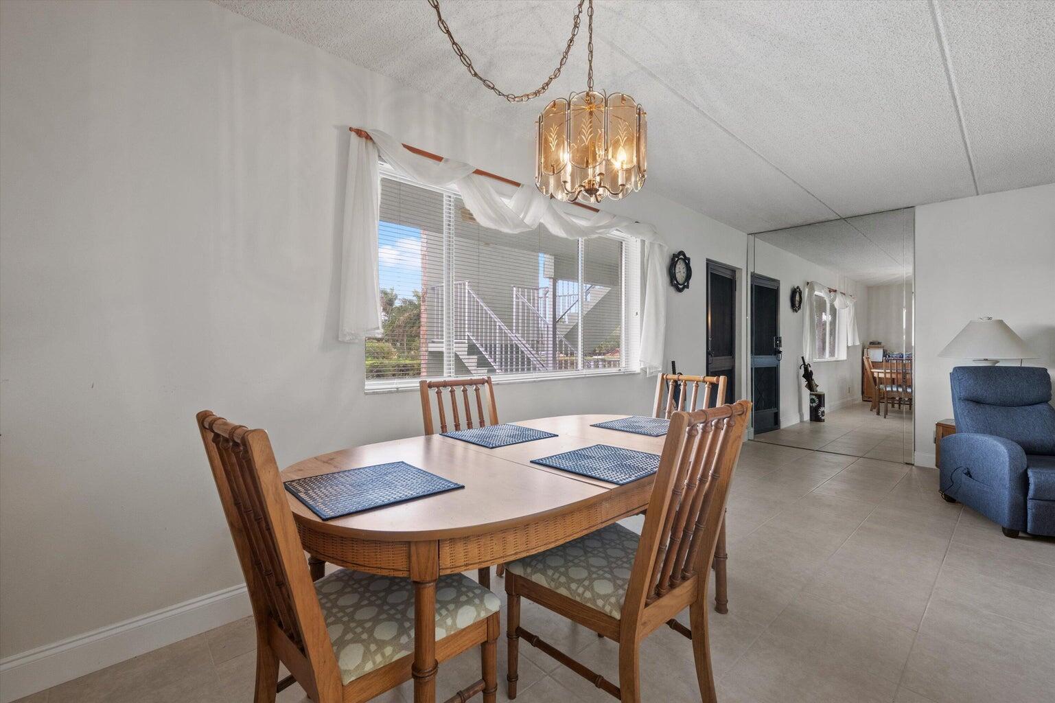A dining area features a wooden table, chairs, a chandelier, and a large mirrored wall — 3300 Springdale Boulevard # 202, Palm Springs FL 33461, PALM SPRINGS, FL