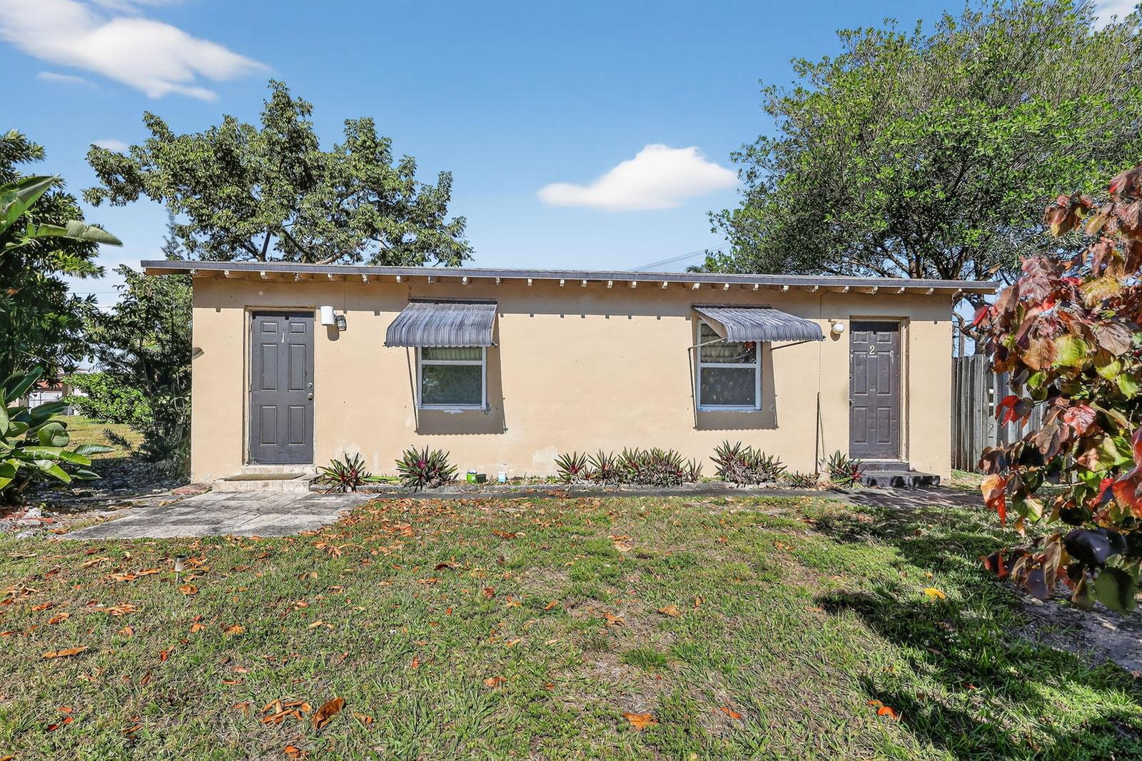A single-story tan stucco duplex with two dark doors and two windows with metal awnings — 411 Columbus Parkway # 5, Hollywood FL 33021, HOLLYWOOD, FL