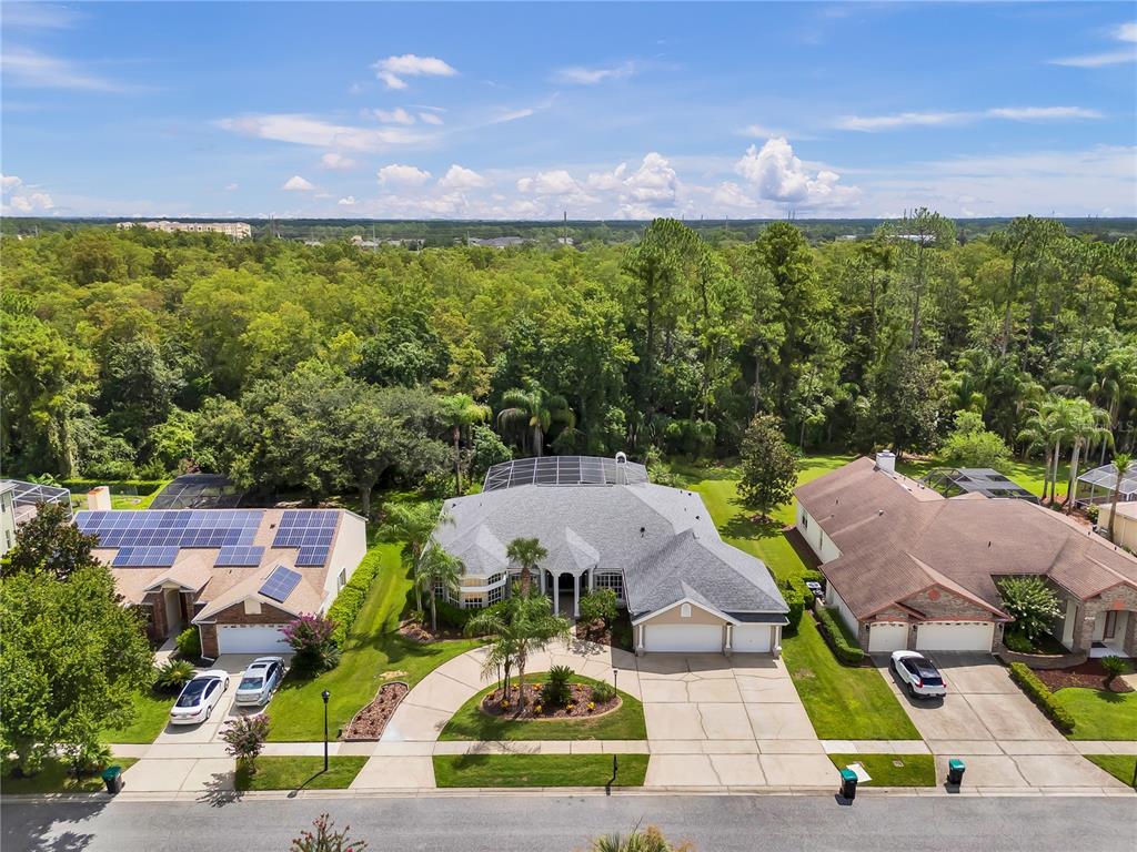 An aerial view shows three suburban houses with driveways, lawns, and a dense forest background — 4749 SUDBURY DRIVE, ORLANDO, FL