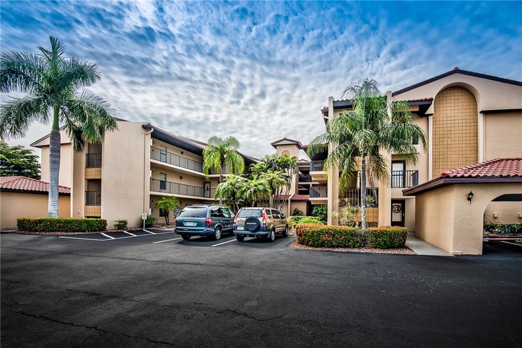 A multi-story apartment building with a parking lot, palm trees, and a cloudy blue sky — 2601 W MARION AVENUE UNIT 47A, PUNTA GORDA, FL