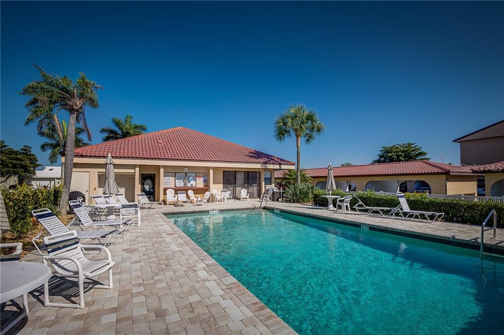 A rectangular swimming pool sits on a paved patio in front of a community clubhouse — 2601 W MARION AVENUE UNIT 47A, PUNTA GORDA, FL