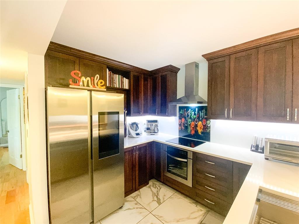 A kitchen features dark wood cabinets, stainless steel appliances, white countertops, and marble-look floor tiles — 3134 LAKE PINE WAY UNIT C2, TARPON SPRINGS, FL