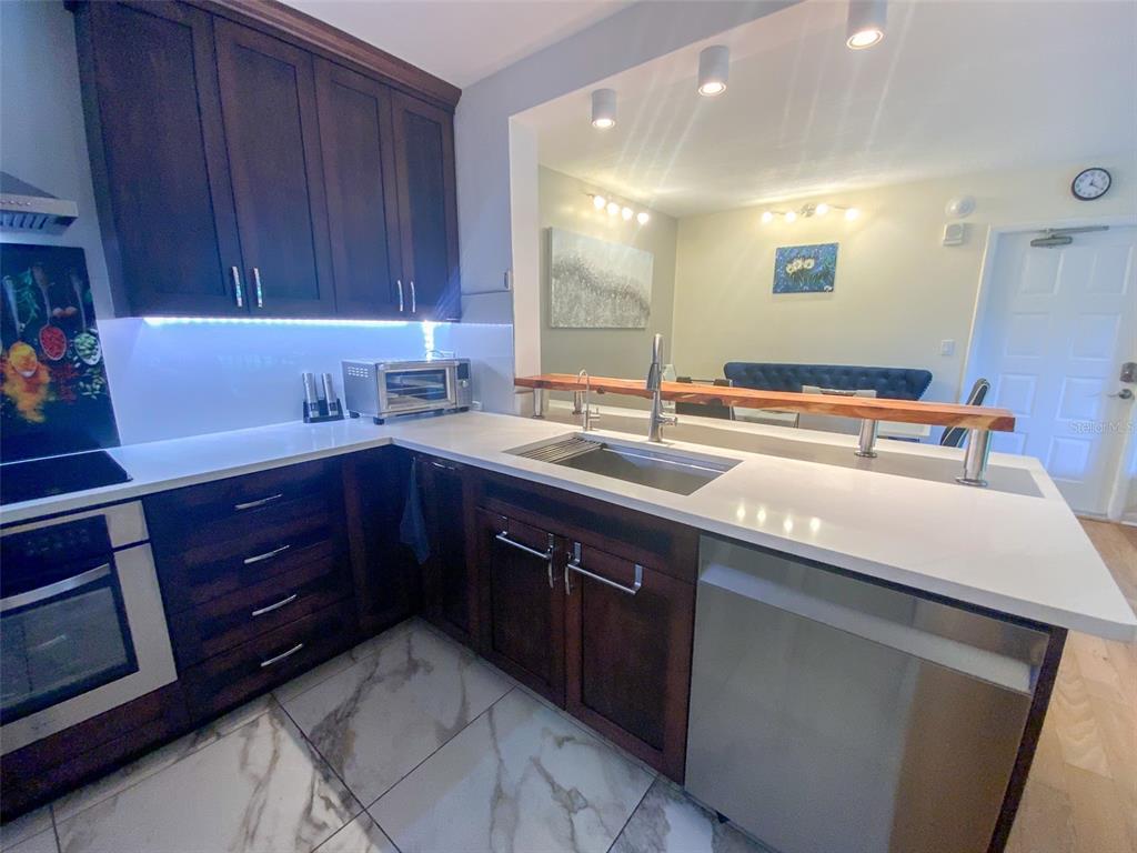 A modern kitchen features dark wood cabinets, white countertops, stainless steel appliances, and tile flooring — 3134 LAKE PINE WAY UNIT C2, TARPON SPRINGS, FL
