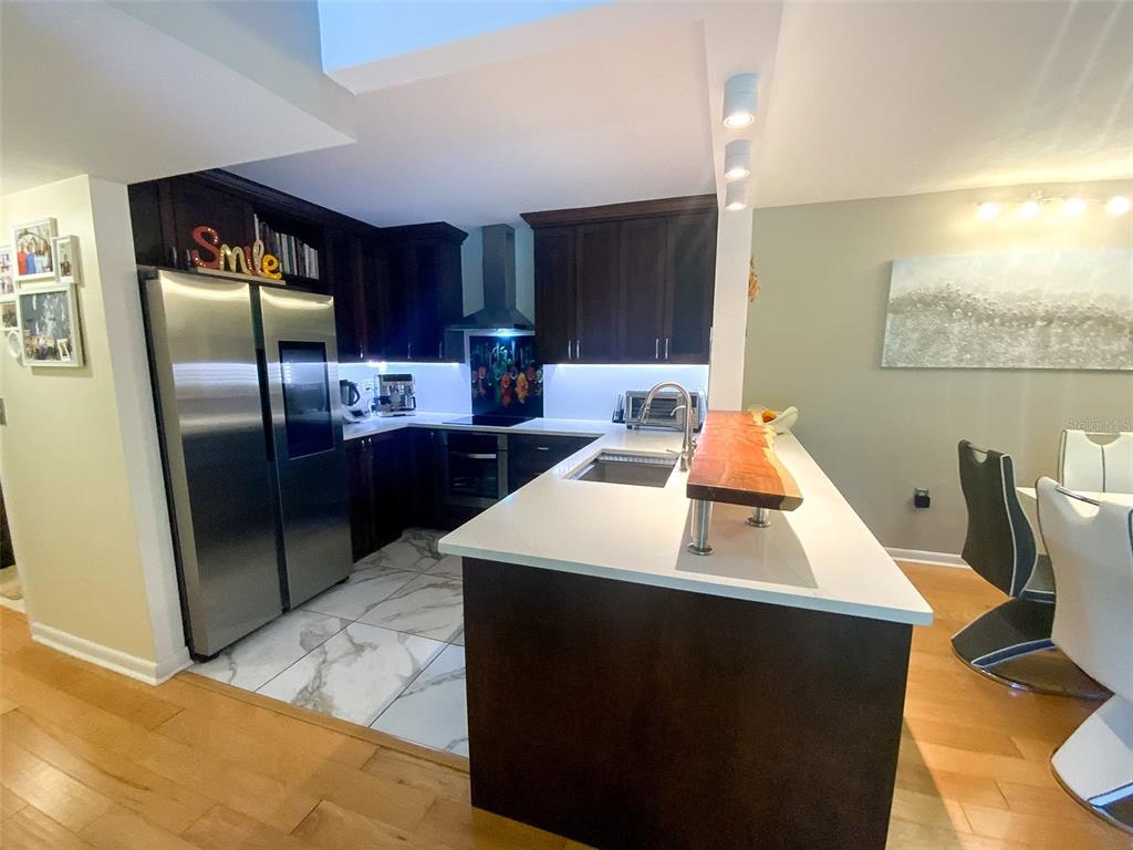 A modern kitchen features dark wood cabinets, white countertops, stainless steel appliances, and marble flooring — 3134 LAKE PINE WAY UNIT C2, TARPON SPRINGS, FL
