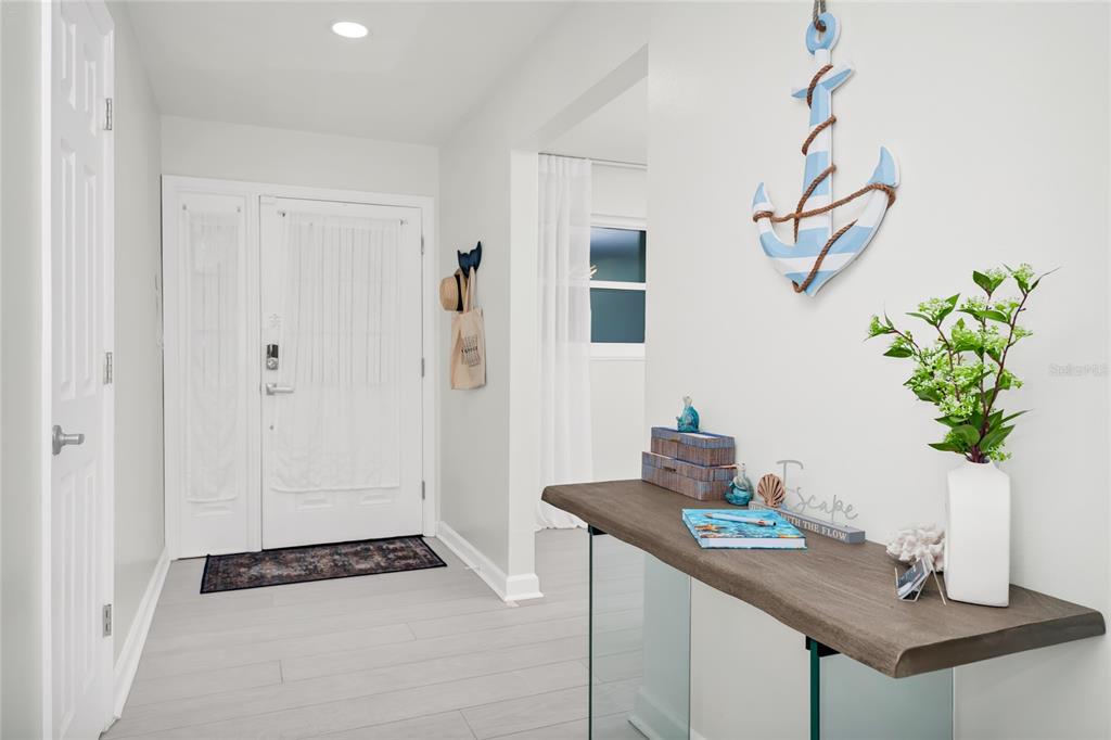 A bright entryway features light wood-look flooring, a white front door, and a coastal-themed console table — 363 HARBOR DR, CAPE CANAVERAL, FL