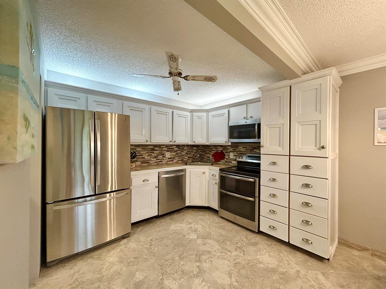 A kitchen features white cabinetry, stainless steel appliances, a tiled backsplash, and light-colored flooring — 223 Pine Hov Circle # 2, FL 33463, FL