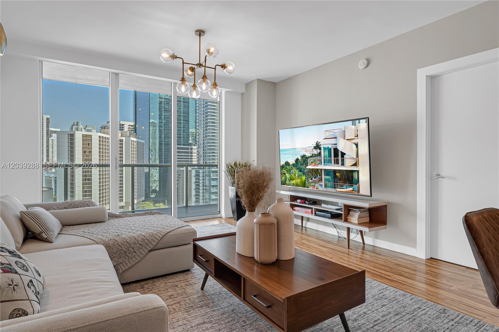 A modern living room features a sectional sofa, wooden coffee table, and city skyline views — MIAMI, FL