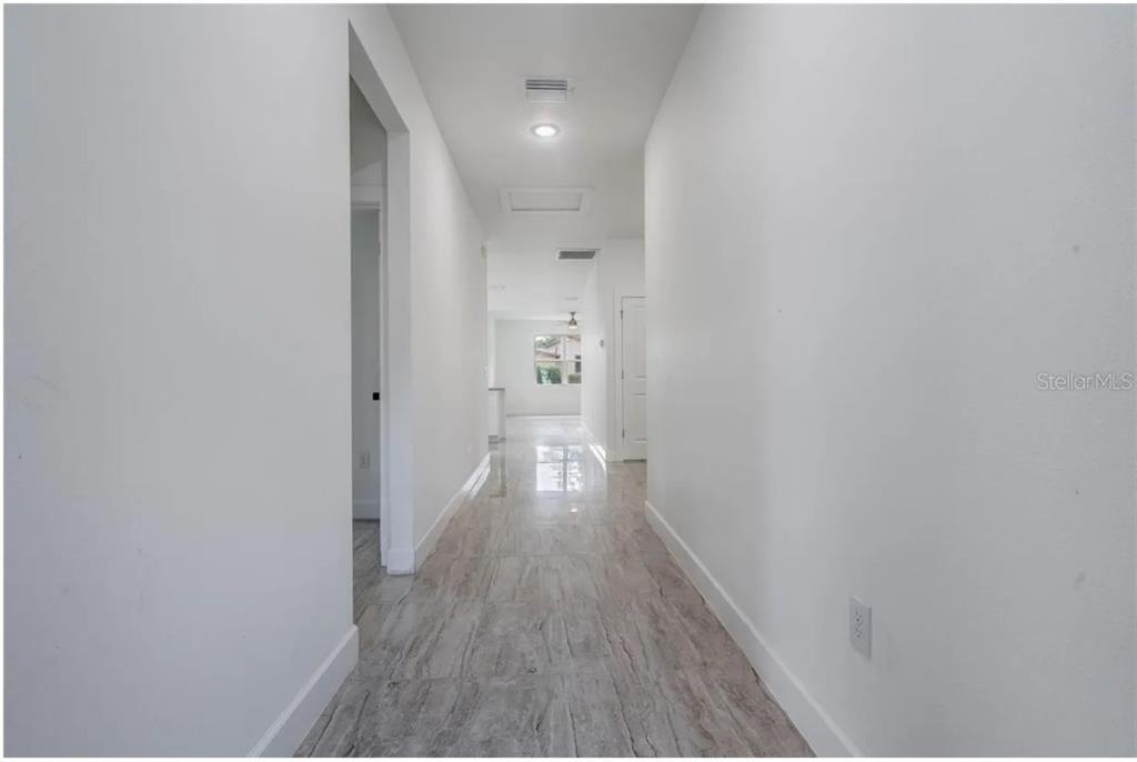 A long hallway with white walls and light-colored tile flooring leads toward an open room — 113 W REDDING STREET, DAVENPORT, FL