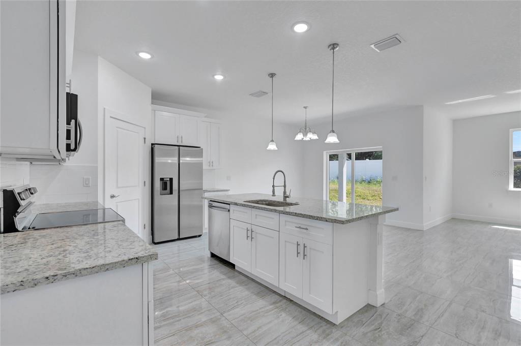 A modern kitchen features white cabinets, granite countertops, stainless steel appliances, and tile flooring — 113 W REDDING STREET, DAVENPORT, FL