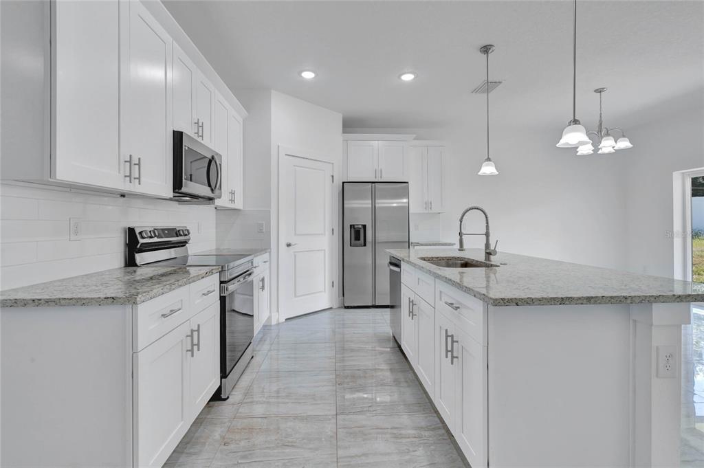 A modern kitchen features white cabinets, granite countertops, stainless steel appliances, and tile flooring — 113 W REDDING STREET, DAVENPORT, FL