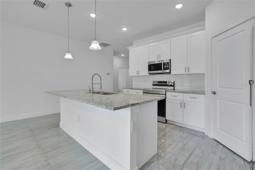 A modern kitchen features white cabinets, granite countertops, a center island, and tile flooring — 113 W REDDING STREET, DAVENPORT, FL