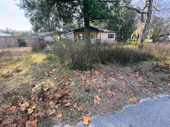 A single-story house with light-colored siding sits behind overgrown vegetation and a large tree — 1522 NE 21ST STREET, OCALA, FL