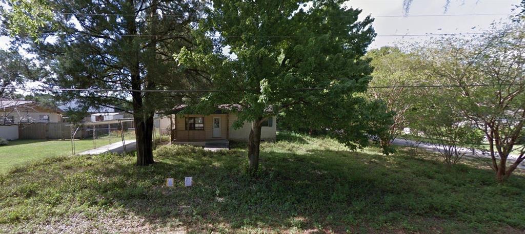 A small, single-story house sits behind large trees on a lot with overgrown vegetation — 1522 NE 21ST STREET, OCALA, FL