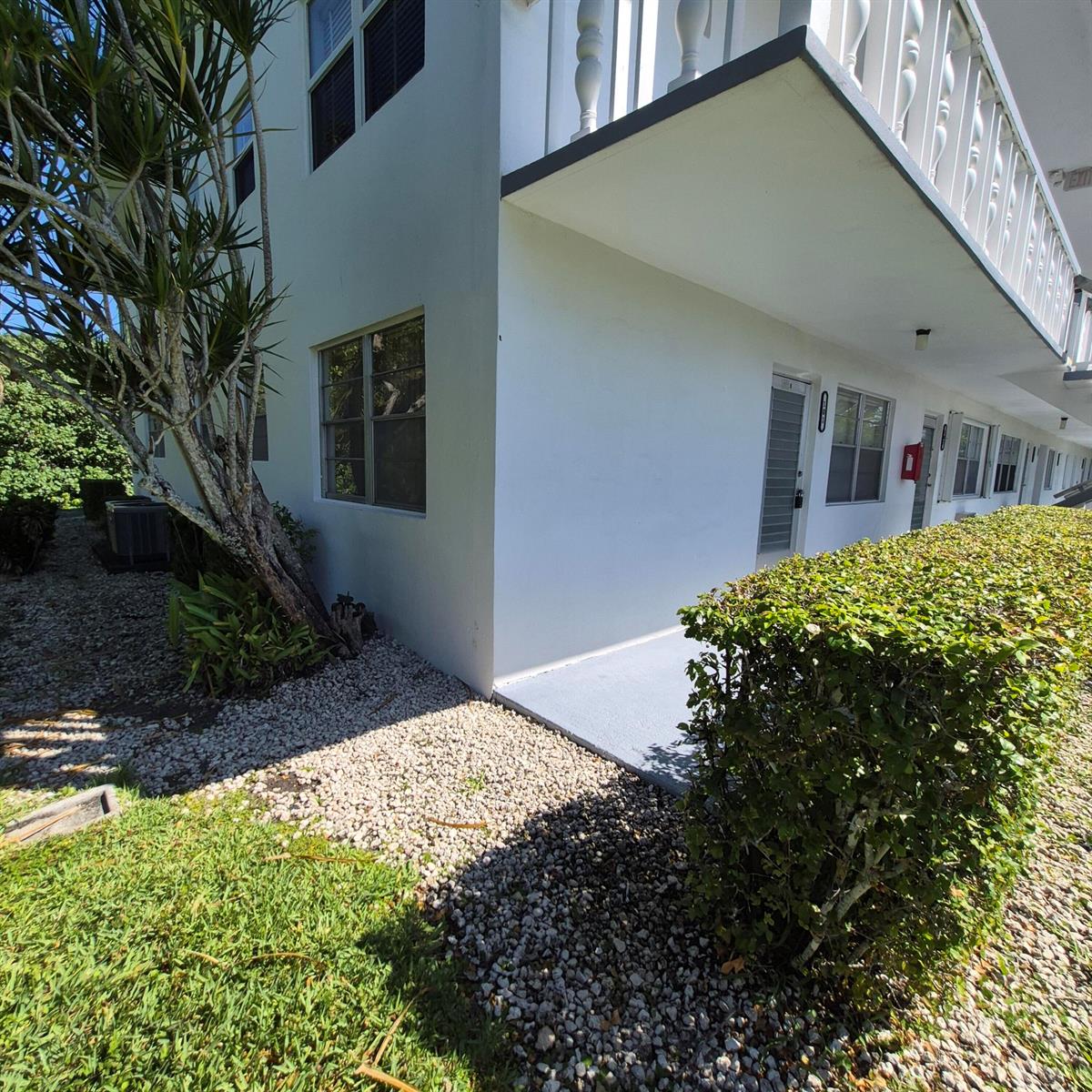 Exterior view of a white multi-story apartment building with a gravel yard and hedge — 101 Northampton F, West Palm Beach FL 33417, WEST PALM BEACH, FL