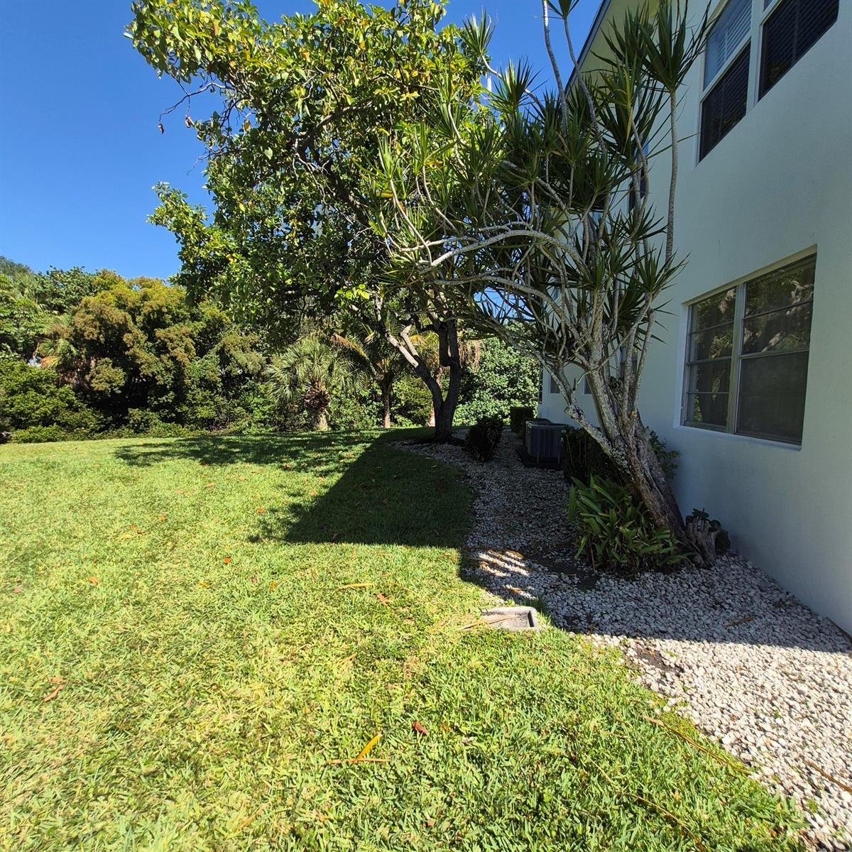 A side view of a white house exterior with a gravel bed and trees — 101 Northampton F, West Palm Beach FL 33417, WEST PALM BEACH, FL