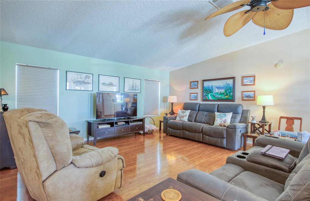 A living room features hardwood floors, a ceiling fan, and gray reclining furniture — 258 PELICAN DRIVE N, OLDSMAR, FL