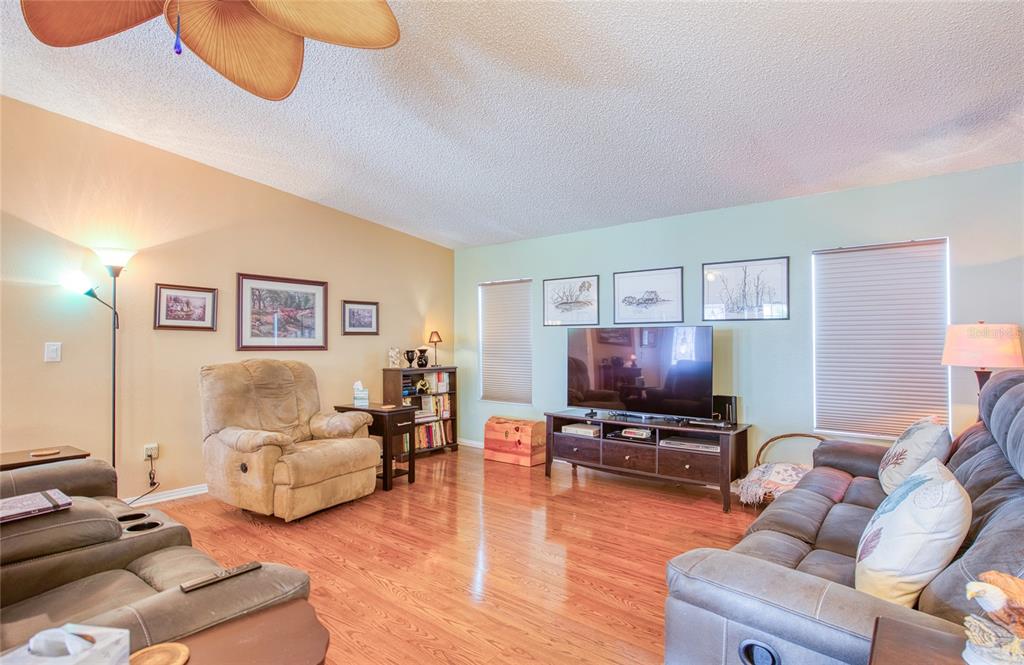 A living room features hardwood floors, a ceiling fan, a television console, and leather furniture — 258 PELICAN DRIVE N, OLDSMAR, FL