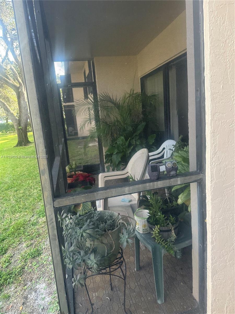 A screened-in patio features potted plants, two plastic chairs, and a view of a lawn — 5851 Washington St # 84, Hollywood FL 33121, HOLLYWOOD, FL