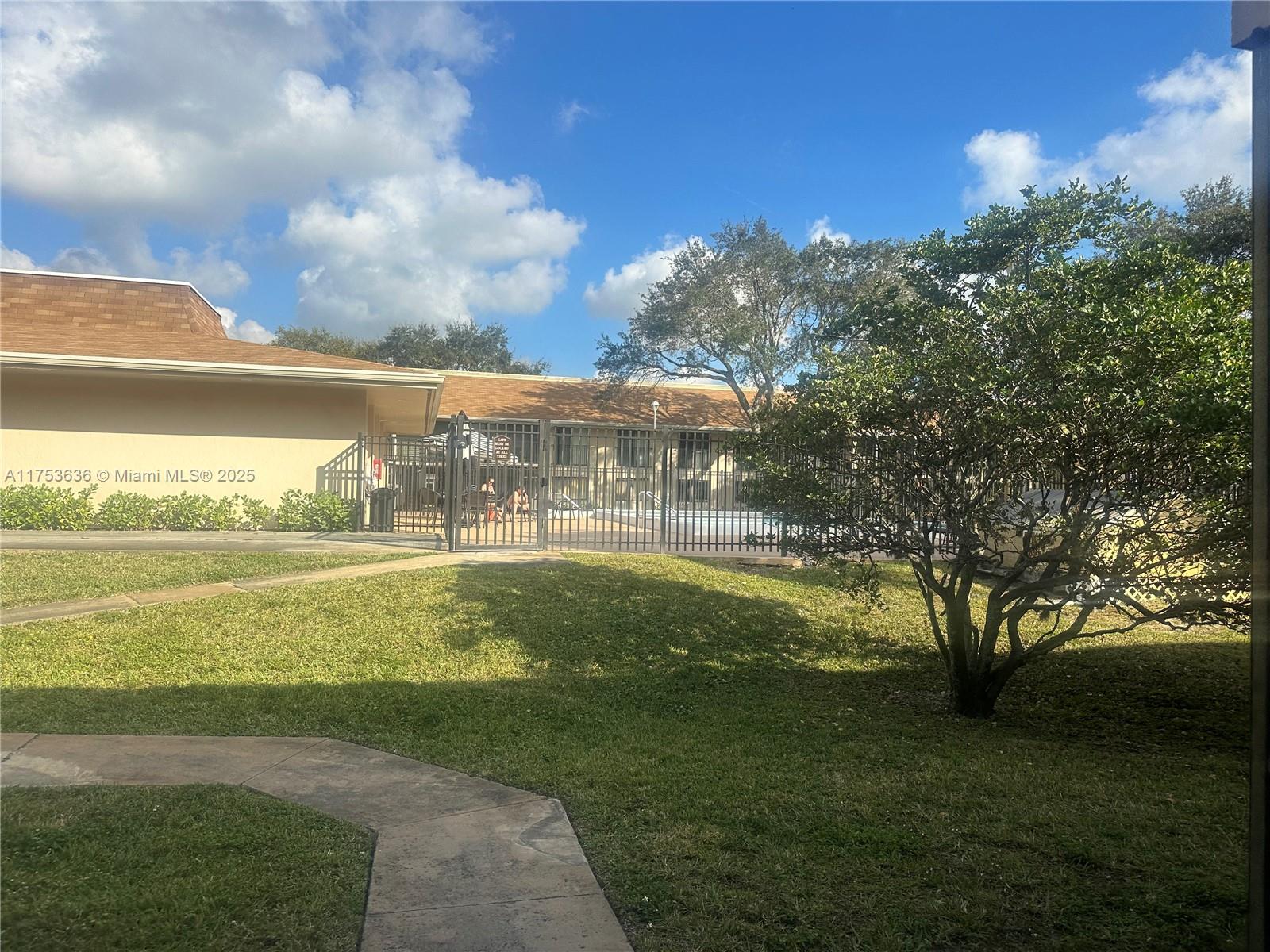 A fenced swimming pool area is situated between two single-story buildings with grassy lawns — 5851 Washington St # 84, Hollywood FL 33121, HOLLYWOOD, FL
