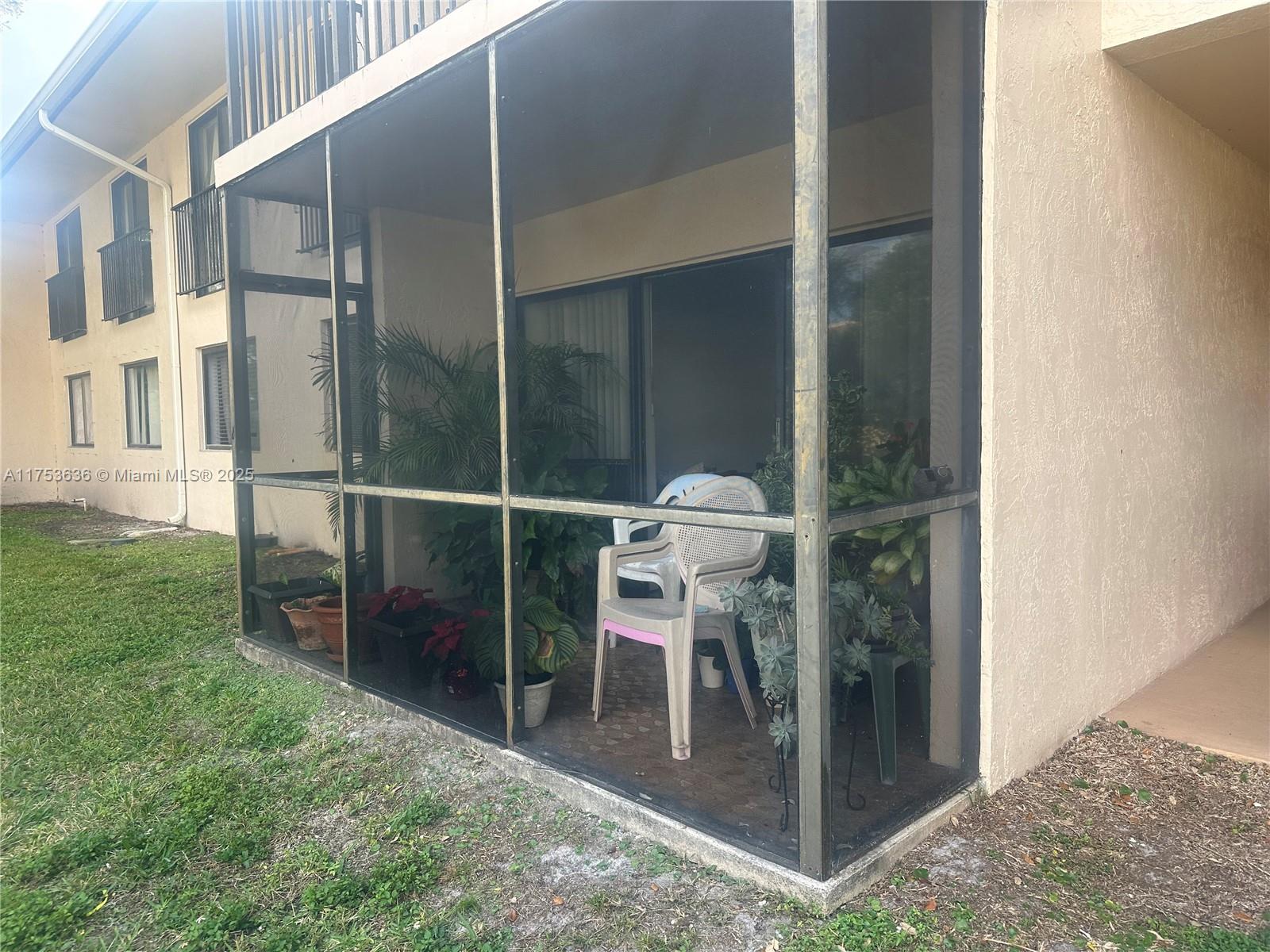A ground-floor screened-in patio features potted plants and plastic chairs next to a building exterior — 5851 Washington St # 84, Hollywood FL 33121, HOLLYWOOD, FL