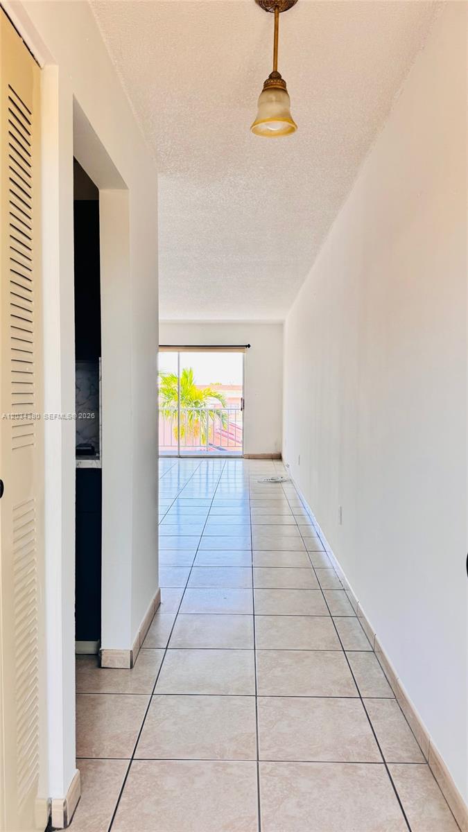 A tiled hallway leads to a living area with a sliding glass door and balcony — 1480 W 46th St # 322, Hialeah FL 33012, HIALEAH, FL