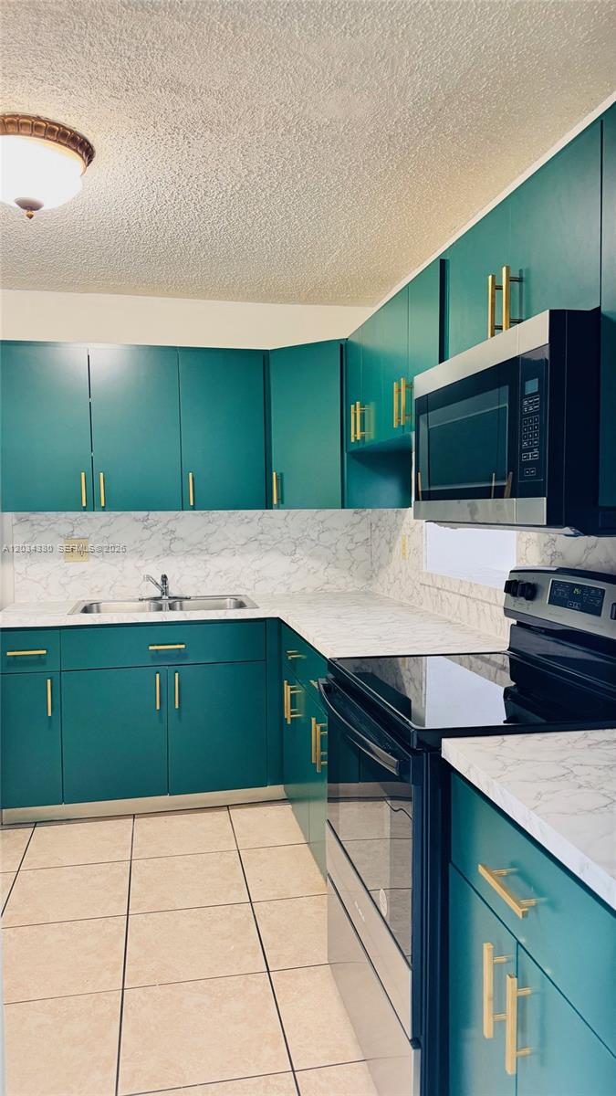 A kitchen features teal cabinets, gold hardware, and white marble-patterned countertops and backsplash — 1480 W 46th St # 322, Hialeah FL 33012, HIALEAH, FL