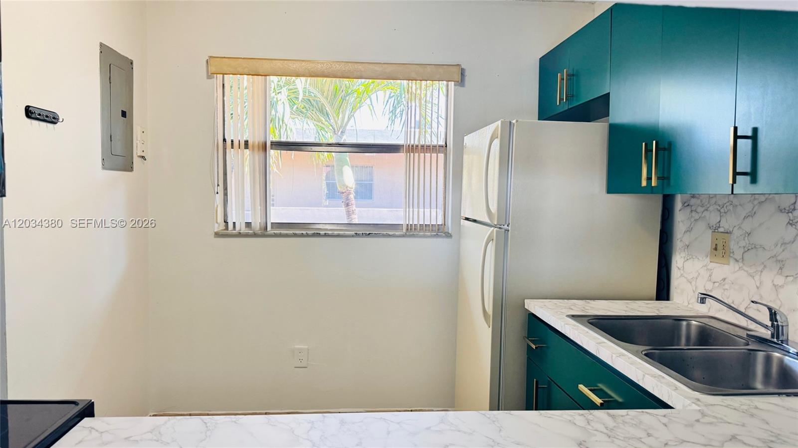 A kitchen features teal cabinets, white marble-patterned countertops, a stainless steel sink, and a window — 1480 W 46th St # 322, Hialeah FL 33012, HIALEAH, FL